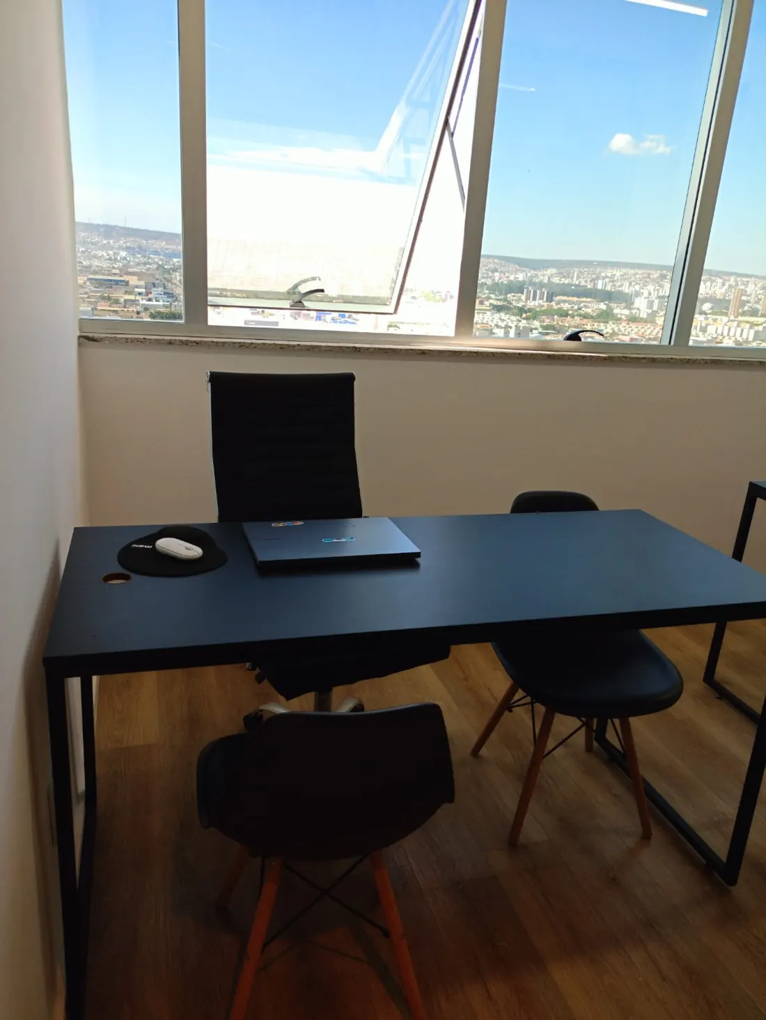 Sala de atendimento com mesa escura, cadeiras e janela com vista para a cidade
